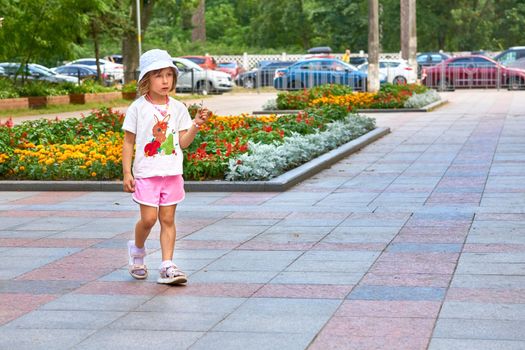 a child or young person. Wonderful serious child walks and city square with flower beds in summer day.