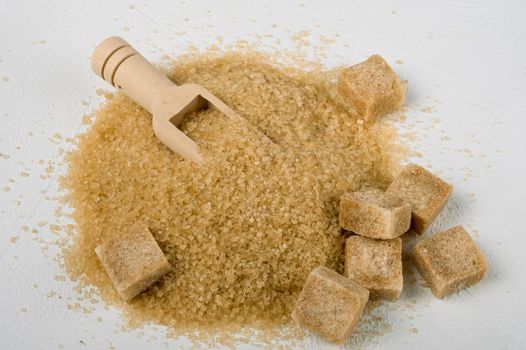 Brown cane sugar is also sprinkled in lumps on a light surface. Wooden scoop for bulk products. Selective focus. Space for text.