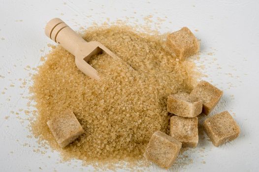 Brown cane sugar is also sprinkled in lumps on a light surface. Wooden scoop for bulk products. Selective focus. Space for text.