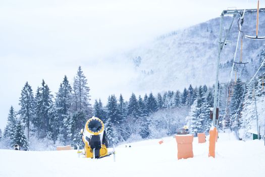 Yellow artificial snow cannon under snow on Wasserkuppe in Rhoen Hesse Germany ski resort on snowy mountain after fresh snow fall. High quality photo