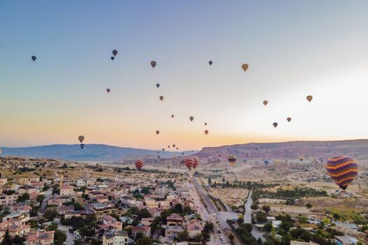 Colorful hot air balloons flying over at fairy chimneys valley in Nevsehir, Goreme, Cappadocia Turkey. Spectacular panoramic drone view of the underground city and ballooning tourism. High quality.