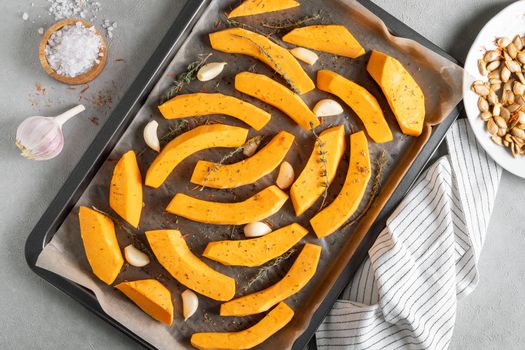 Pieces of ripe pumpkin prepared for baking in the oven. Pumpkin on a baking sheet with olive oil, garlic and dry thyme on the kitchen table. Healthy food. View from above. Selective focus.