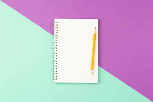 Open spiral notebook with pencil on two color background. Top view, flat lay.