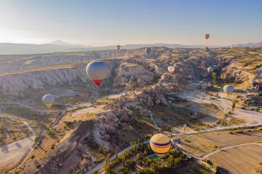 Colorful hot air balloons flying over at fairy chimneys valley in Nevsehir, Goreme, Cappadocia Turkey. Spectacular panoramic drone view of the underground city and ballooning tourism. High quality.