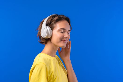 Positive woman listening music, enjoying with headphones on blue studio background. Radio, wireless modern sound technology, online player. High quality photo