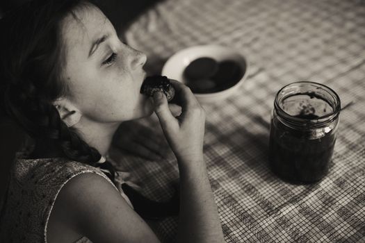 Cute funny toddler girl eats sweet bun for breakfast. Happy child eating bread roll with strawberry jam. Health food for children and kids with selfmade jelly. High quality photo