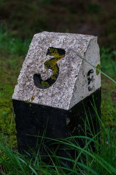 A black and white stone sign with the number three by the road close up