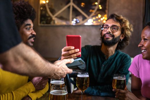 Man paying bill in a bar with phone. Friends paying round of drinks with mobile phone at pub. Technology and leisure concept.