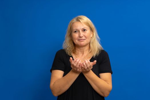 Closeup portrait of a smiling, happy excited beautiful woman with raised palms arms in you offering something, isolated over blue background. Positive emotion facial expression sign symbols