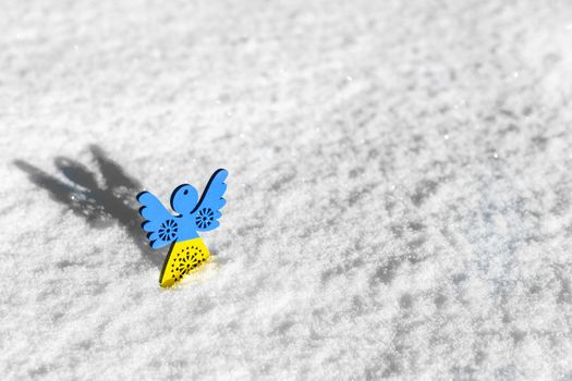 yellow blue wooden angel on white snow as a symbol of support for ukraine in winter. concept needs help and support, truth will win