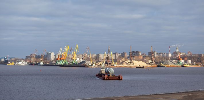 River port. Port cranes on the bank of the river. Embankment of the river port, a barge at the quay wall. Large port cranes on the river. Extraction and transportation of sand other cargo