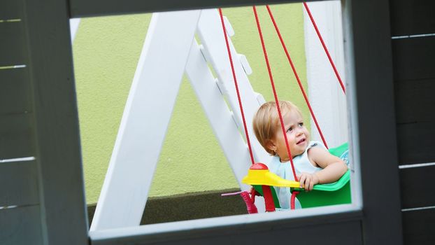 summer, in the garden, nice little one year-old girl swinging on a swing in the playground. High quality photo