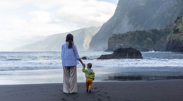 Mother and little child holding hands walking at sea side. High quality photo