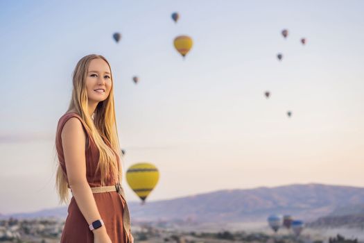 Tourist woman looking at hot air balloons in Cappadocia, Turkey. Happy Travel in Turkey concept. Woman on a mountain top enjoying wonderful view.