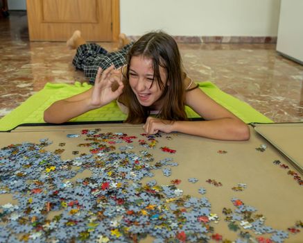 Pretty brunette girl lying on the floor arranging pieces of a puzzle game. Playing board game at home