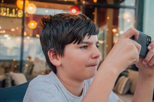 Portrait of young boy playing mobile phone games in a bar, with concentrated expression.