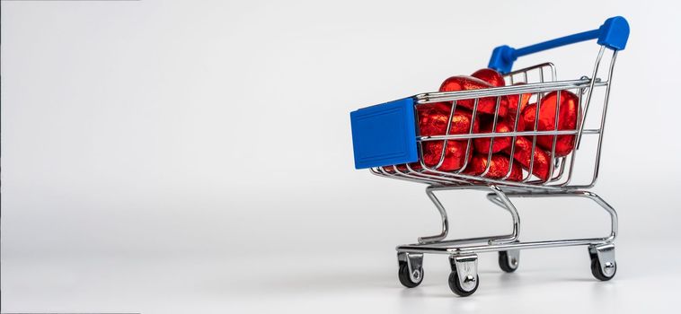 Supermarket trolley loaded with heart-shaped candies on a white background. Gifts and purchases for the New Year and Christmas. Online trading. toy shopping cart carries candy. Love concept: heart shape candies. valentine's day