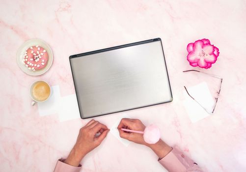 an office worker in a pink shirt sits at a laptop, top view, next to a cup of coffee and a donut. High quality photo