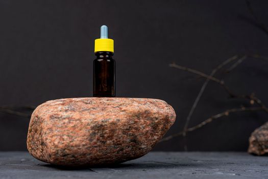 dropper bottle for cosmetics stands on a natural stone, black background. A glass dropper bottle with a pipette. Nature Skin concept. Skincare cosmetic. Beauty concept for face body care. Organic Spa Cosmetics