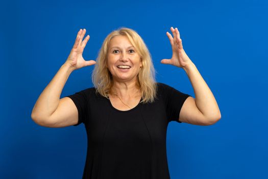 Attractive surprised woman, lady, woman, model, person, looking forward with raised hands smiling. Isolated on blue background with copy space.