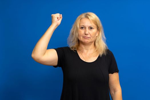 Close-up portrait of her pretty, attractive, charming, cute, cheerful, successful, straight-haired girl showing strong arm muscle isolated on blue toned background