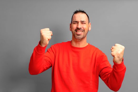 Portrait of bearded latino man in his 40s celebrating success with fists up and eyes closed isolated over gray background