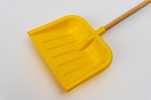 bright yellow plastic children's snow shovel with wooden handle on white background. High quality photo