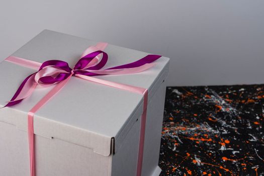 a large white gift box tied with a red ribbon on a spotted colored background gift box with a red satin bow. space for copying. A birthday gift with love. A box for holiday gifts. side view from above