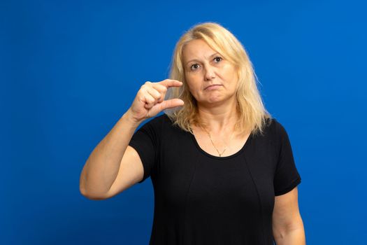 It needs a little more. Portrait of displeased skeptical woman gesturing, undersized, dissatisfied with low rating. Indoor studio shot isolated on blue color background