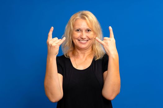 Beautiful blonde woman over blue isolated background screaming with crazy expression doing rock symbol with hands up. Music star. Heavy concept.
