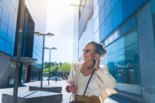 Attractive middle aged business woman smiling talking with her smart phone in the street. High quality photo