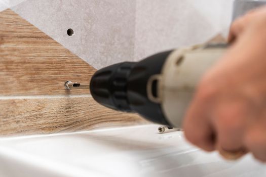 drilling holes in porcelain stoneware, drilling holes in tiles. Close-up of drilling a hole with a special cooled drill in a ceramic tile in the bathroom. a worker in the bathroom drills holes in the porcelain tile with a drill to install shelves. home renovation.