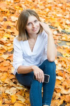 Portrait of a beautiful caucasian girl sitting on falling yellow leaves and smiling, autumn leaf fall, High quality photo