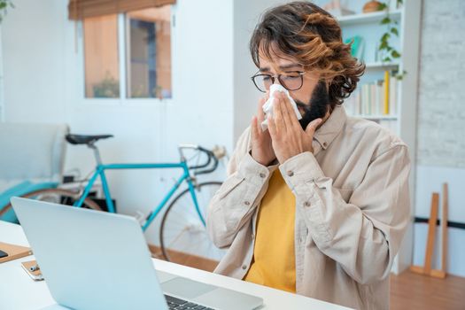 Ill at work young man got flu allergy sneezing blowing wiping running nose in tissue - allergic guy caught cold at job sitting at home office workplace having respiratory disease sick leave concept. High quality photo