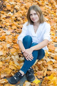 Portrait of a beautiful caucasian girl sitting on falling yellow leaves and smiling, autumn leaf fall, High quality photo