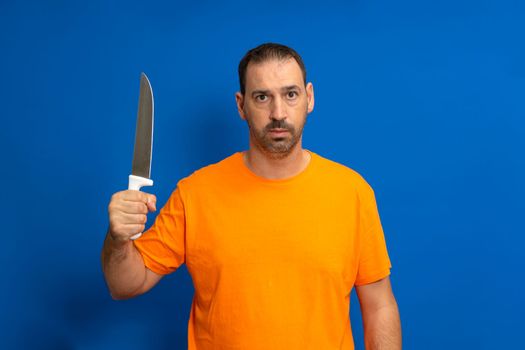 Caucasian man with beard holding kitchen knife with threatening and dangerous attitude, confident gesture looking serious.