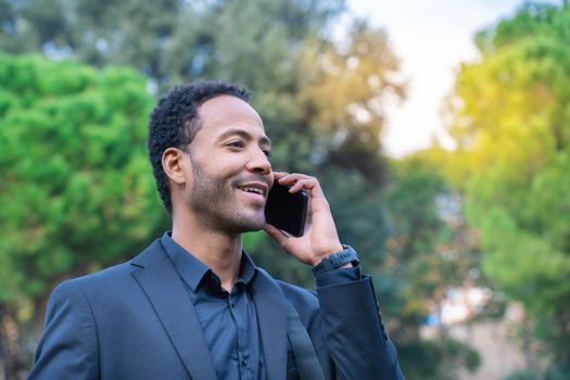 Close up portrait of attractive young black man talking on mobile phone outdoors. High quality photo