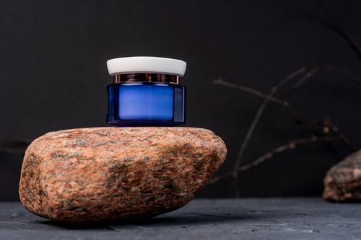 a mock-up, a round purple plastic jar with a white lid for cosmetics stands on a natural stone, black background. Natural creams and masks. Product branding. Organic cosmetics concept