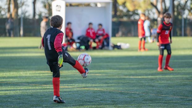 Boy goalkeeper kicking soccer ball on sports field in a match