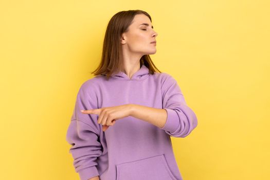 Get out. Portrait of upset vexed woman showing exit, demanding to leave her alone, has resentful irritated expression, wearing purple hoodie. Indoor studio shot isolated on yellow background.