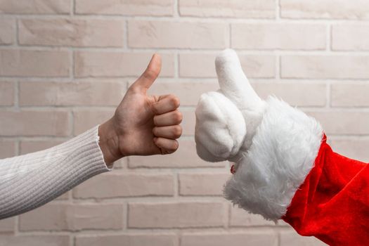 Santa and the girl give a thumbs up on the background of a light brick wall. New Year's greetings. Christmas holiday greeting. A gesture from Santa. Close-up