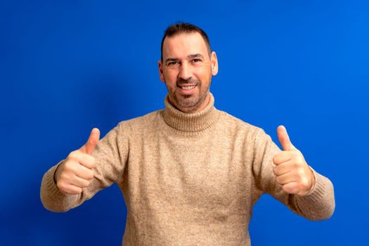 Handsome man wearing brown turtleneck giving thumbs up positive hand gesture smiling and happy for success. Winning gesture.