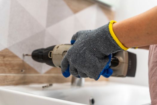 drilling holes in porcelain stoneware, drilling holes in tiles. Close-up of drilling a hole with a special cooled drill in a ceramic tile in the bathroom. a worker in the bathroom drills holes in the porcelain tile with a drill to install shelves. home renovation.