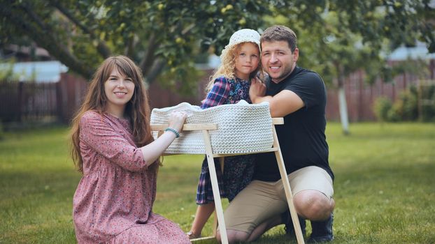 A young family looks at their newborn baby in a cradle in the garden