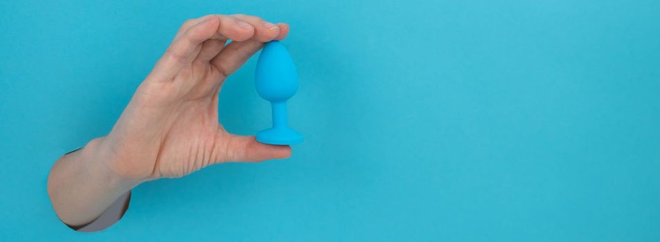 Woman holding a blue anal plug on a blue background. Widescreen