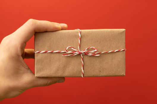 hand holding craft wrapped gift over red background. High quality photo