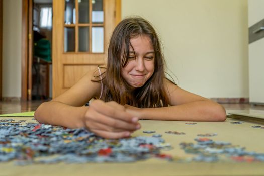 Teenage brunette girl doing puzzle lying on the floor of her house, she spends time running away from technology and enjoying traditional games