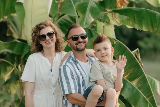 Father, mother, and son are having fun with palm trees in the background. A close photo of a laughing family in the park in summer at sunset.