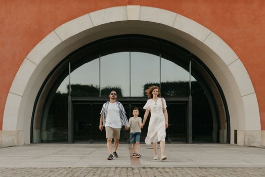 Father, mother and son are strolling from the arch in an old European town. A happy family is holding hands in the evening.