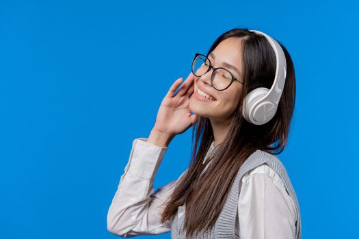 Happy student teenager listening music, enjoying dance with headphones on blue studio backdrop. Radio, wireless modern sound technology, online player. Copy space. High quality photo